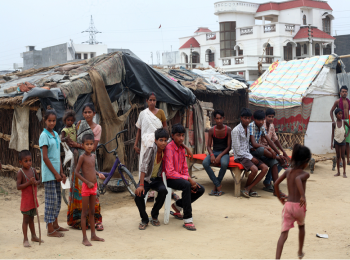 A slum with its residents in front of it and a big house behind to indicate wealth inequality